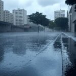 Rua urbana no Sudeste do Brasil durante chuva intensa, com nuvens escuras e poças d'água.