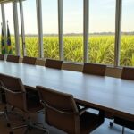 Sala de reuniões vazia com vista para campos agrícolas no Brasil, representando encontro sobre agronegócio.