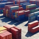 Porto brasileiro com contêineres e navios, representando queda de 25,5% nas exportações para EUA e déficit de US$ 700 milhões.