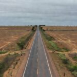Rodovia federal no Paraná com cercas e campos agrícolas sem cultivo.